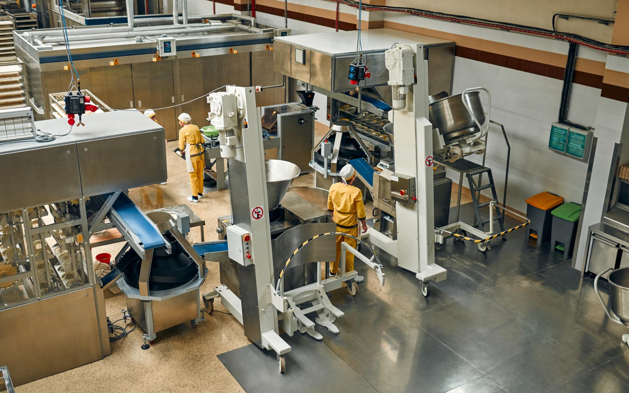 Producción automatizada en la industria alimentaria Fábrica de alimentos con maquinaria automatizada y operarios supervisando el proceso de producción en una planta de procesamiento industrial.