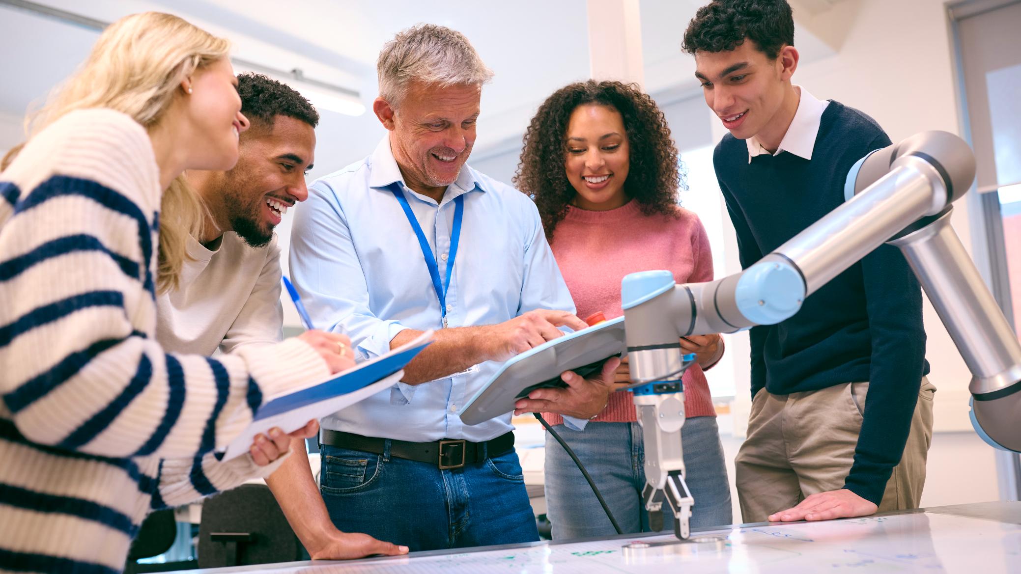 estudiantes-investigando-robotica-colaborativa Grupo de estudiantes universitarios aprendiendo sobre robótica colaborativa con la guía de un profesor, utilizando un brazo robótico en un laboratorio de ingeniería.