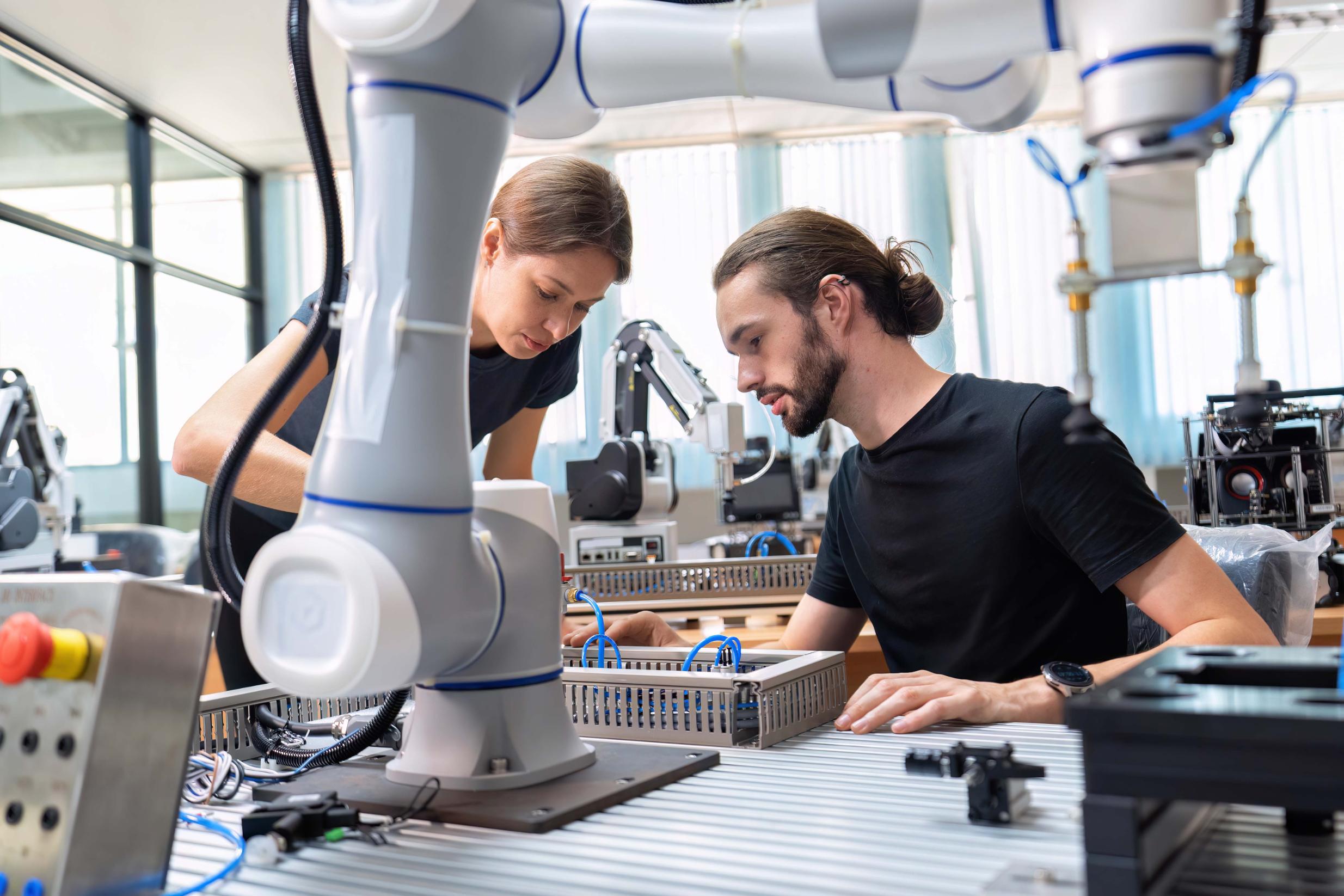 Dos ingenieros trabajando en el desarrollo e integración de un brazo robótico en un laboratorio de robótica industrial.