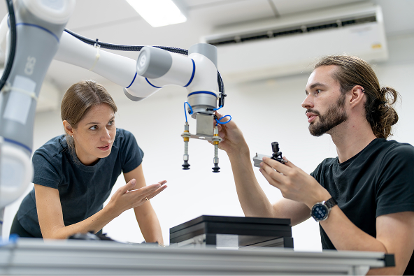 sobre-nosotros Dos ingenieros trabajando con un robot colaborativo en un laboratorio de automatización e investigación tecnológica.